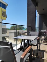 Un balcón con mesa y sillas, con vista a un edificio y un cielo despejado.