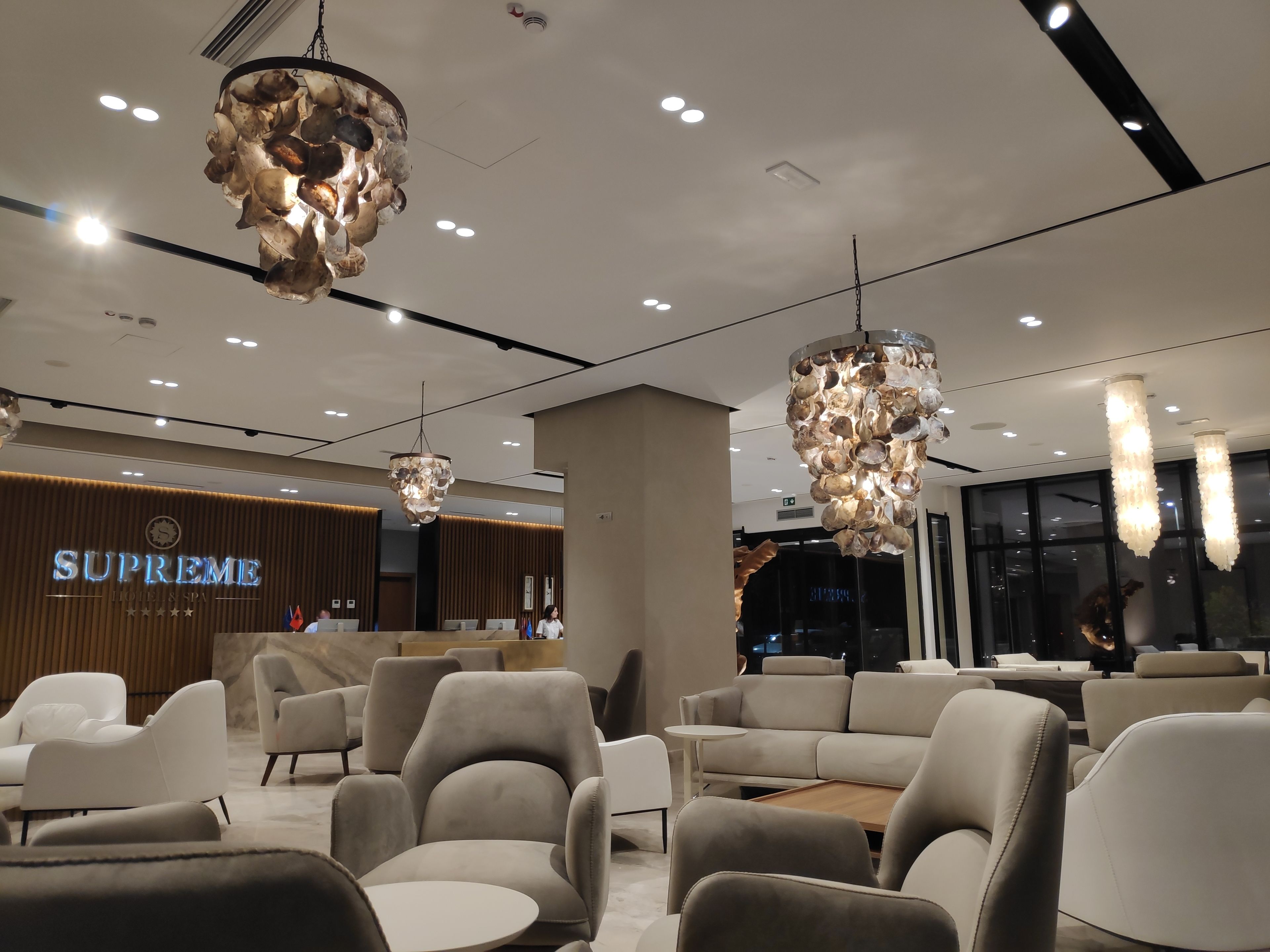 Un hall d’hôtel moderne doté d’un comptoir d’accueil, d’un espace salon et de lustres originaux.