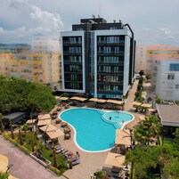Un hotel moderno con una amplia piscina exterior, varios balcones y zonas de estar al aire libre.