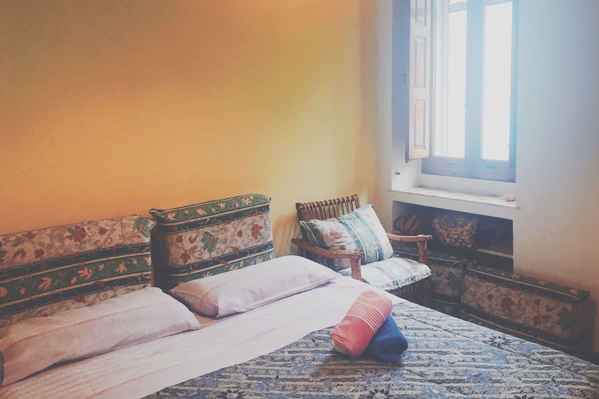 Ein Schlafzimmer mit einem Bett, Kissen, einem Fenster und einem Holzstuhl.