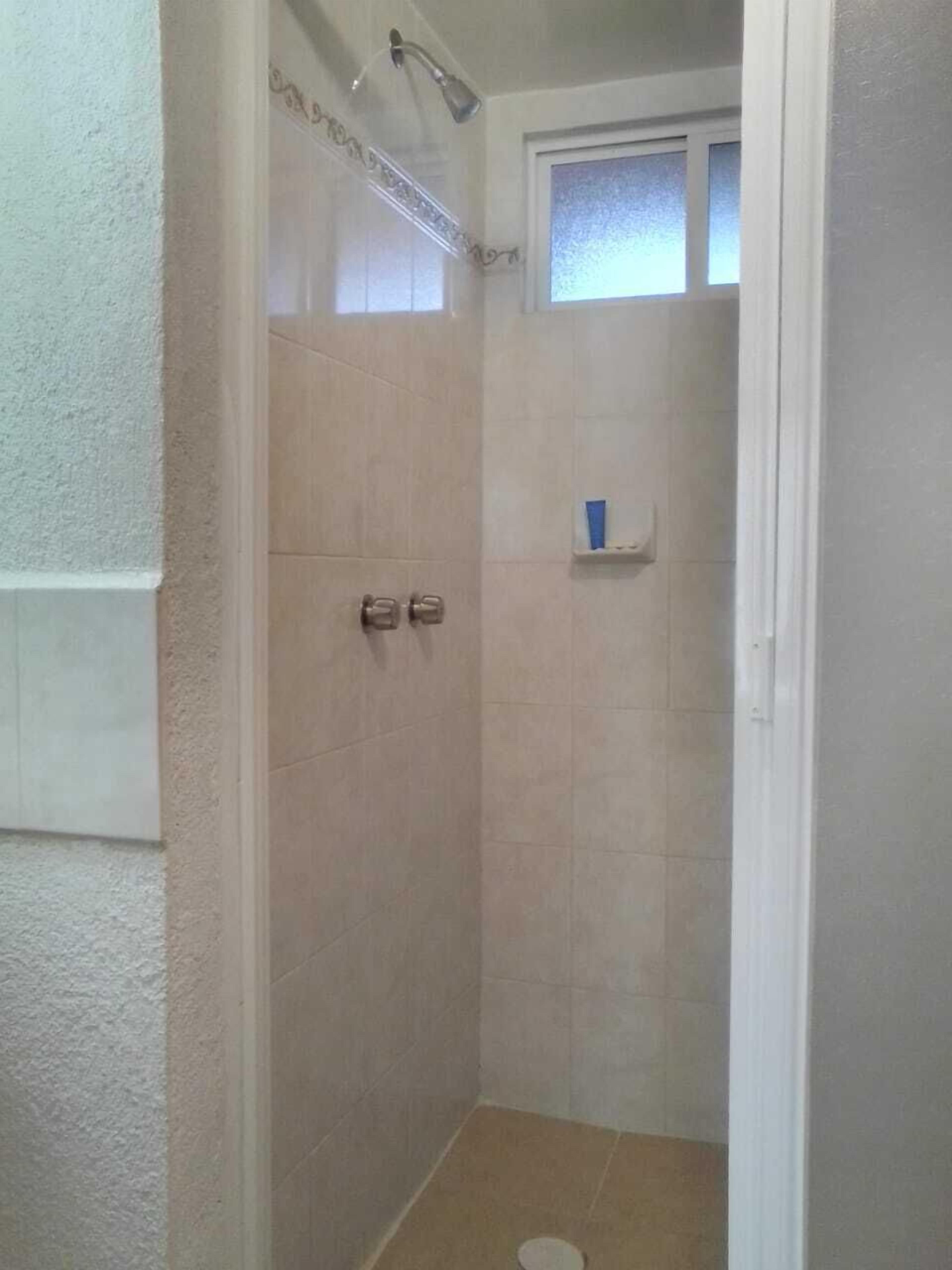 A small, enclosed shower area with a window, a shelf with toiletries, and a door.