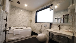A modern bathroom with a marble wall, a large mirror, a bathtub, a toilet, and a sink. - Hotel  Options Lawns (Shahpura)