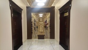 A hallway with marble flooring, a statue in the center, and wooden doors on either side. - Hotel  Options Lawns (Shahpura)