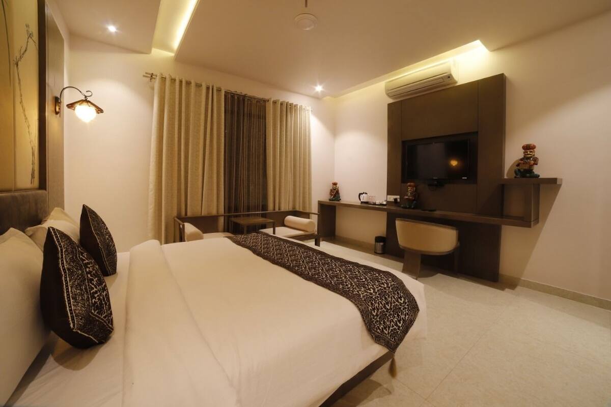 Quarto de hotel moderno com uma cama grande, escrivaninha, cadeira, televisão e banheiro.