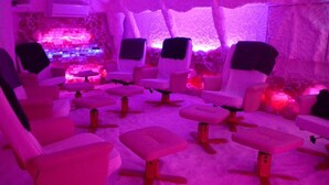 A room with multiple massage chairs arranged in rows, a stone wall, and a pink ambient light. - Hotel Monte Cristo (Hoeselt)