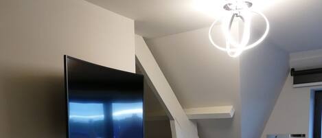 Un interior moderno con un televisor de pantalla plana montado en la pared, una lámpara circular original y una escalera que lleva a otro nivel.