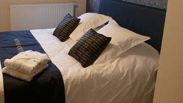 A neatly made bed with white linens, two patterned pillows, and a folded towel on a dark-colored bedspread.