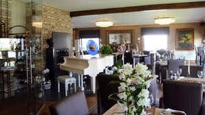 A restaurant with a brick wall, a piano, and multiple dining tables with chairs. - Hotel Monte Cristo (Hoeselt)