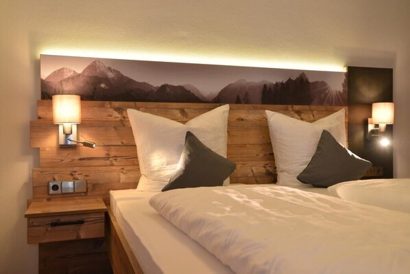 Ein Hotelzimmer mit einem hölzernen Kopfteil, zwei Betten, einem Nachttisch, einer Lampe und einer Wandleuchte.