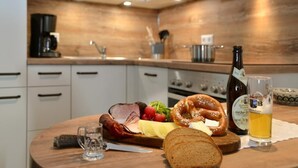 Une table en bois, une planche de charcuterie, une bouteille de bière et un verre de bière.