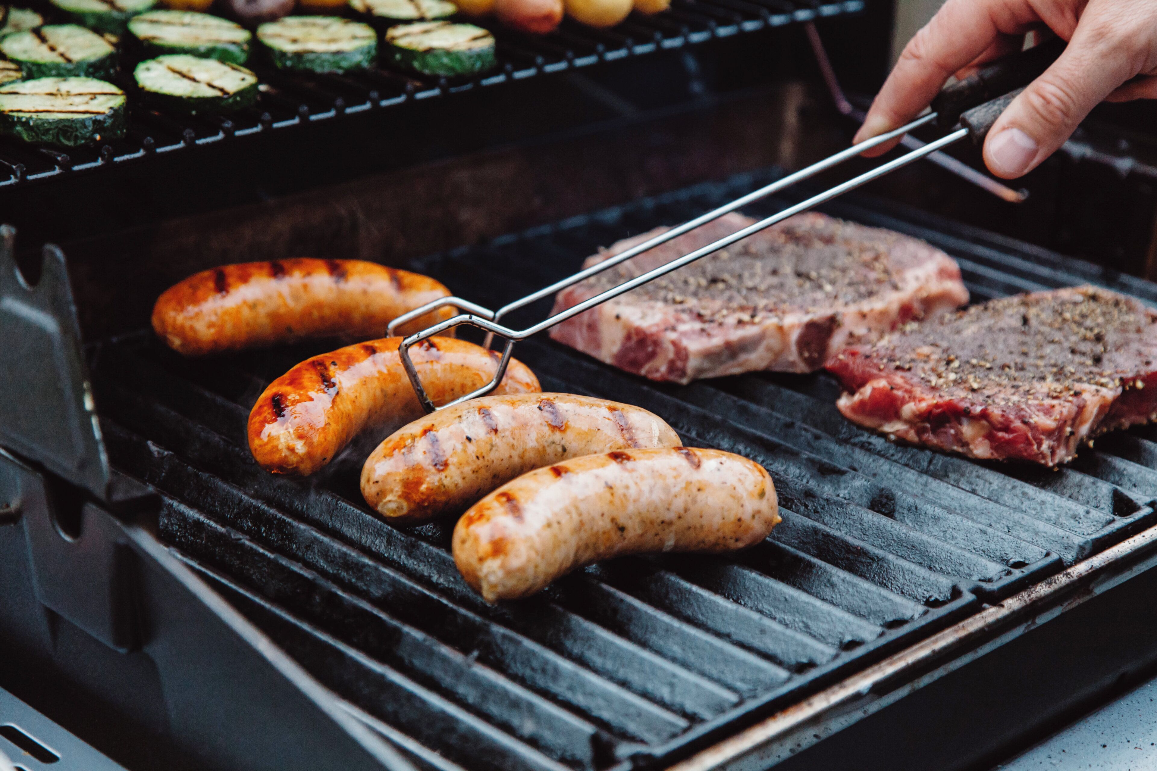 A grill with sausages and meat being cooked.