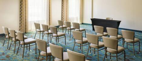 A conference room with rows of chairs, a podium, and large windows with curtains.