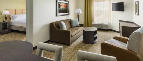 Una habitación de hotel con cama, sofá, mesa de comedor y televisión.