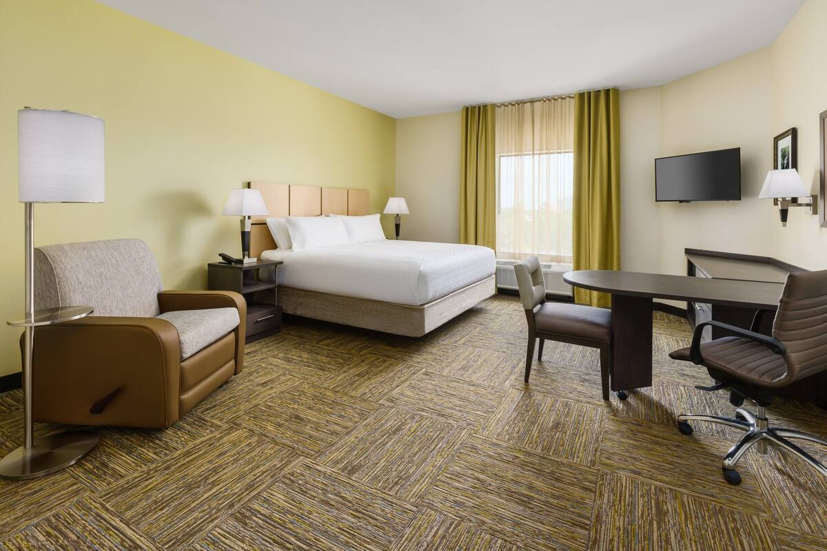 Une chambre d’hôtel avec un lit, deux chaises, un bureau, une télévision et une lampe.