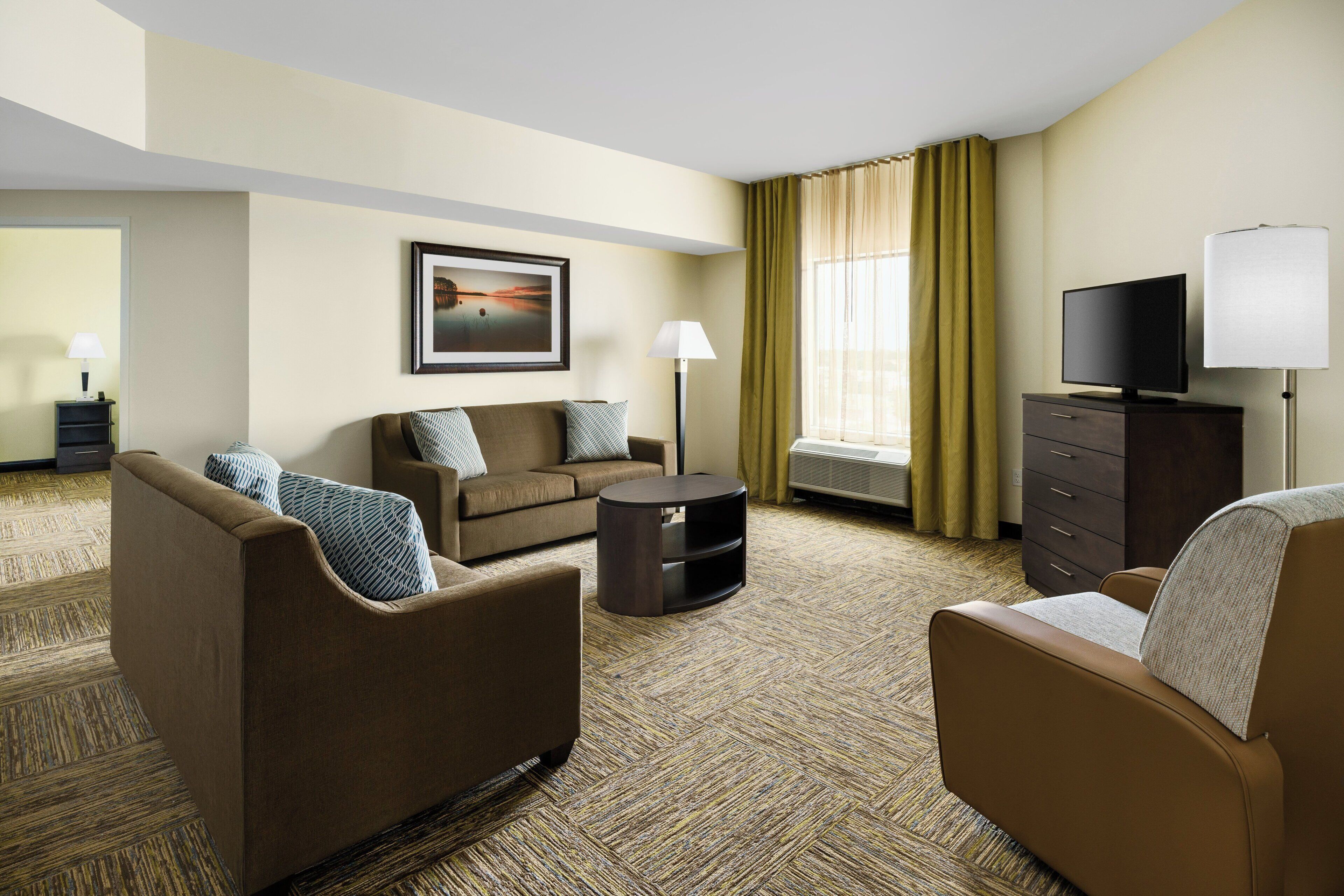 A hotel room with a sofa, armchair, TV, and a framed picture on the wall.