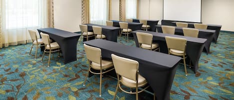 A conference room with tables and chairs, a projector screen, and patterned carpet.