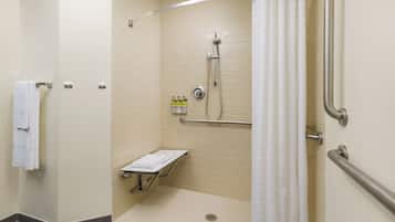 Cabina de ducha accesible para personas con movilidad reducida, con barra de apoyo, perchero y estante con artículos de aseo.