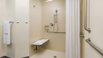 Cabina de ducha accesible para personas con movilidad reducida, con barra de apoyo, toallero y estante con artículos de aseo.