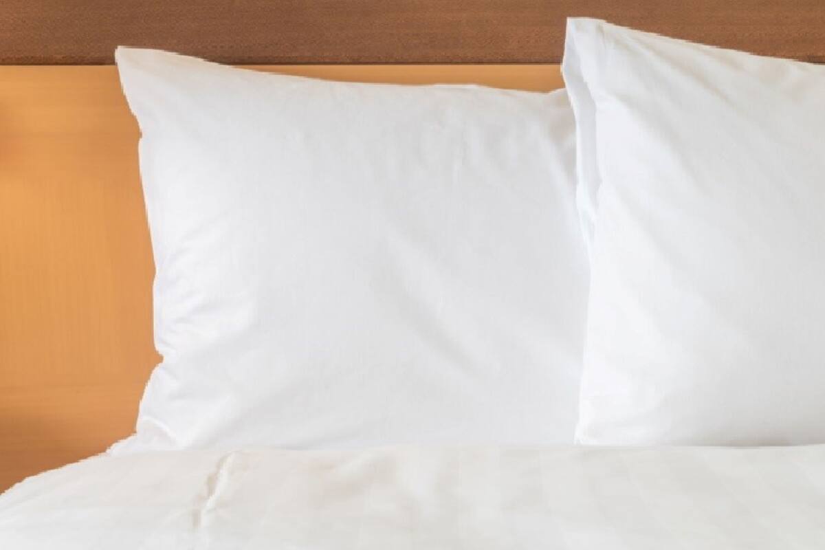 Un lit avec une literie et des oreillers blancs, adossé à une tête de lit en bois.