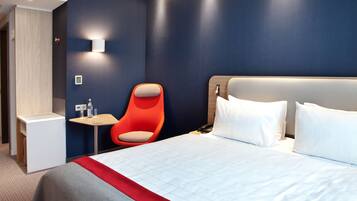 Ein modernes Hotelzimmer mit einem großen Bett, einem kleinen Tisch, einem roten Stuhl und einer Wandleuchte.