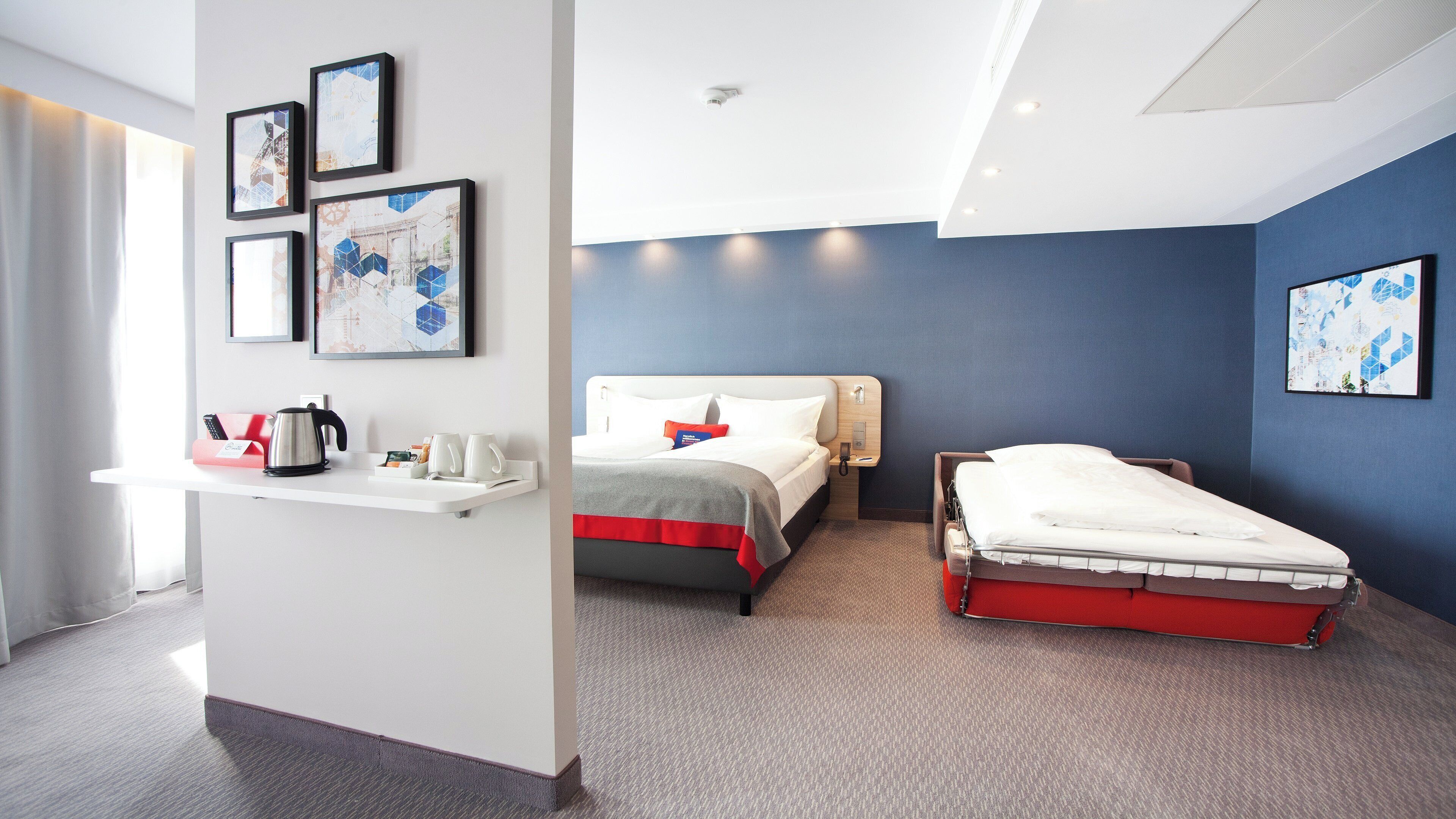 Una habitación de hotel con cama, mesita de noche y escritorio, además de tetera y cafetera.