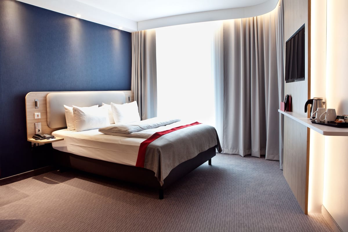 Een moderne hotelkamer met een groot bed, nachtkastje, flatscreen televisie en bureau met koffiezetapparaat.