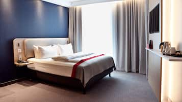 A modern hotel room with a large bed, a bedside table, a flat-screen TV, and a desk with a coffee maker.