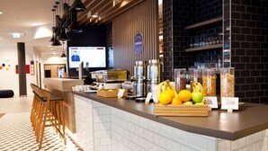 A modern hotel reception area with a counter, bar stools, and a display of fruits and snacks. - Holiday Inn Express Saarbrucken by IHG (Saarbrücken)