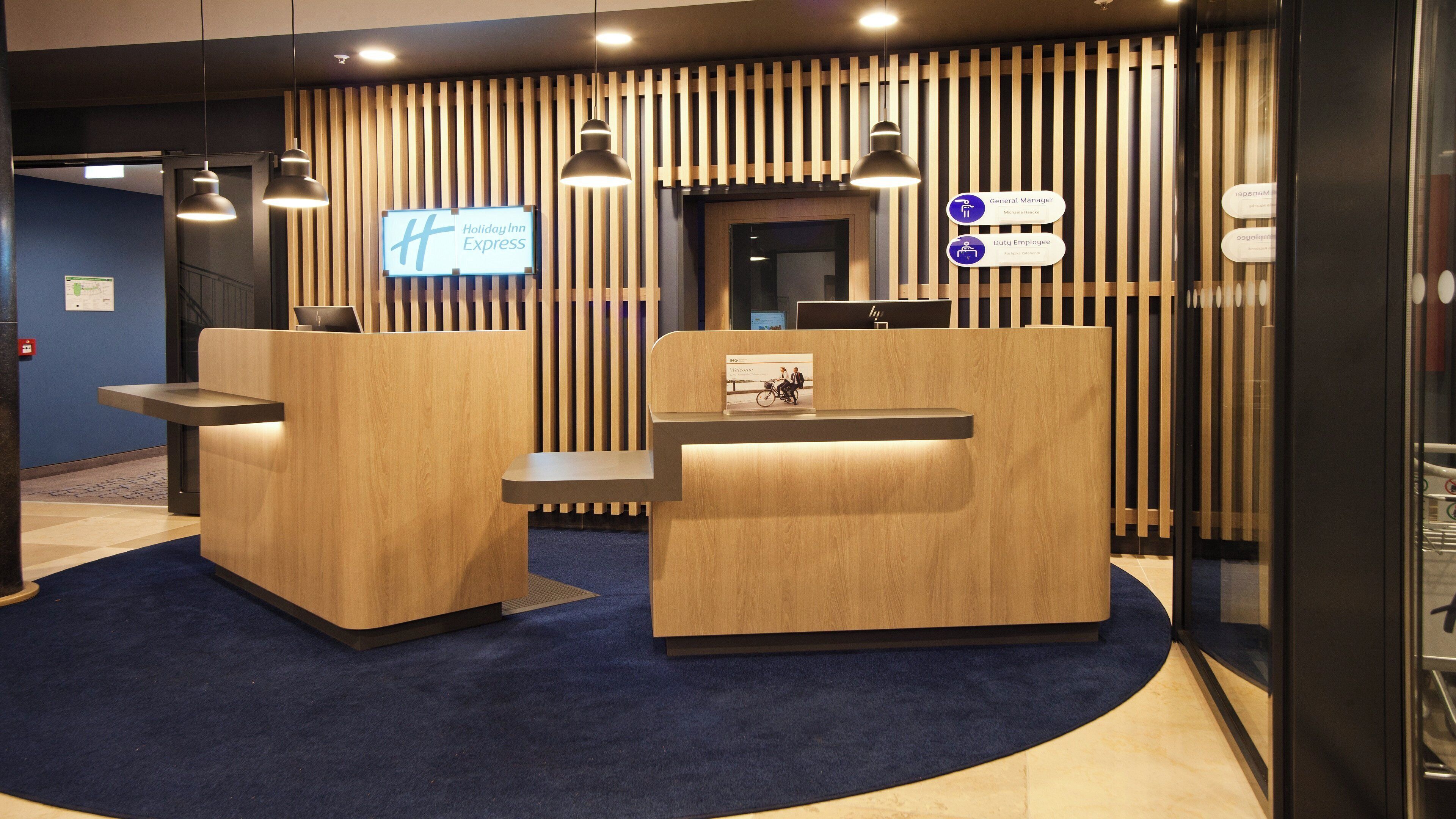 A reception area with two wooden reception desks, a digital display, and a sign indicating a general manager and duty employee.