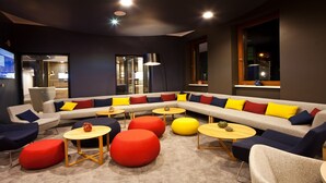 A modern lounge area with a sectional sofa, round tables, and colorful ottomans. - Holiday Inn Express Saarbrucken by IHG (Saarbrücken)