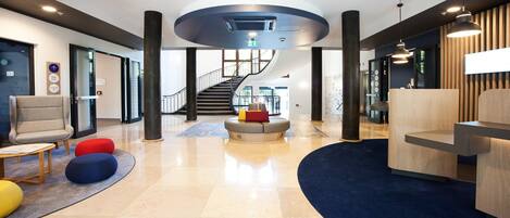 Un lobby moderno con una zona de estar central, una escalera y un mostrador de recepción.