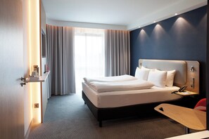 Een moderne hotelkamer met een groot bed, nachtkastje en een bureau met stoel.