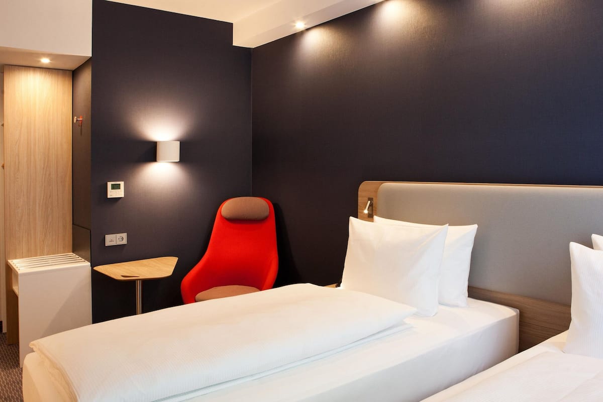 Een hotelkamer met een bed, een rode stoel, een kleine tafel en een wandlamp.