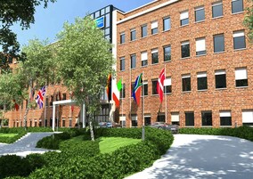 A modern brick building with multiple windows and a landscaped garden with neatly trimmed hedges and a paved walkway.