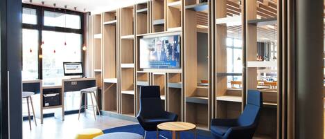 A modern lobby with a large screen displaying news, comfortable seating, and a view of the outdoors.