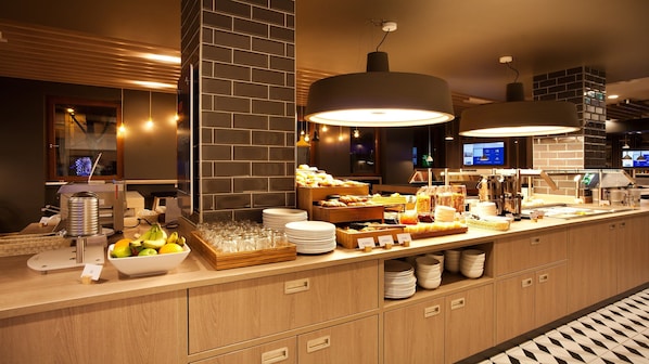 A buffet setup with various food items, glassware, and a television screen in the background.