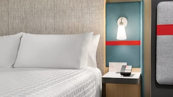 A hotel room with a bed, a nightstand with a phone, and a wall-mounted light fixture.
