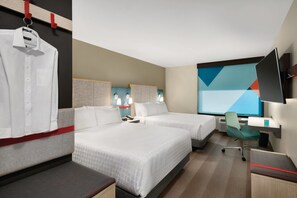 Ein Hotelzimmer mit zwei Betten, einem Schreibtisch, einem Sessel, einem Fernseher und einem Fenster mit geometrischer Aussicht.