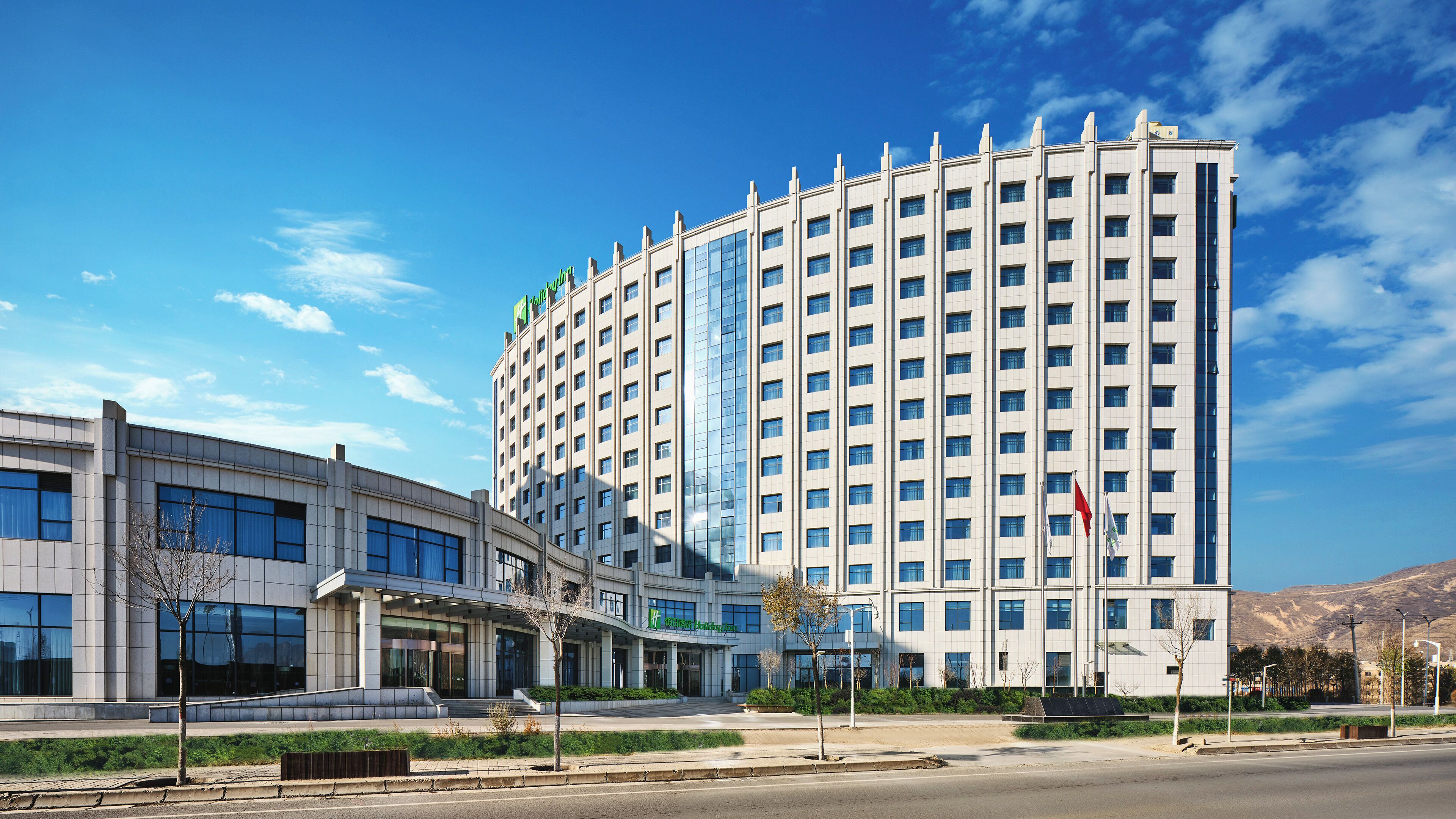 A modern hotel with a prominent glass facade, multiple floors, and a flat roof.