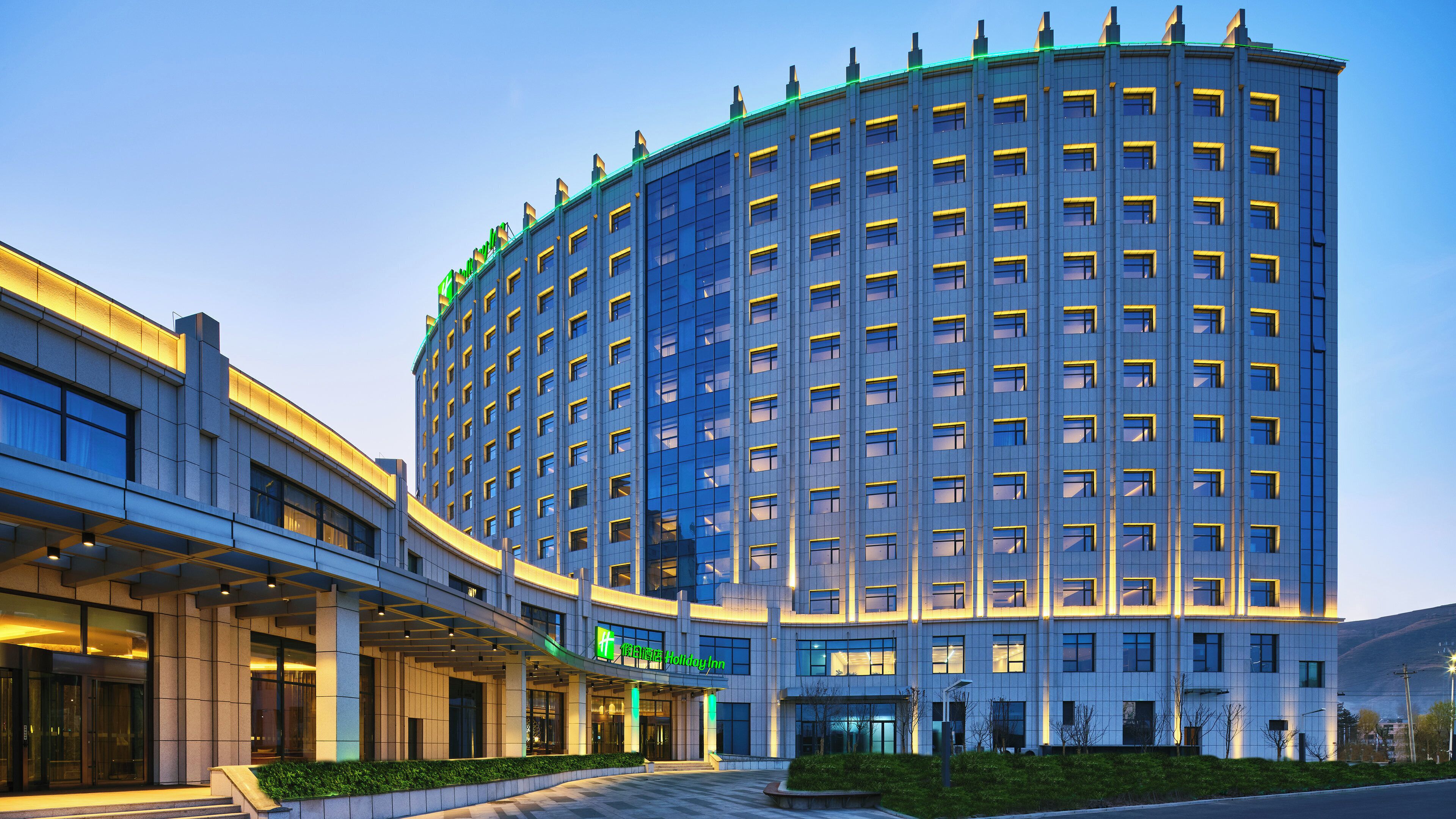 Un hotel de varios pisos con fachada curva, amplias ventanas y una entrada bien iluminada.