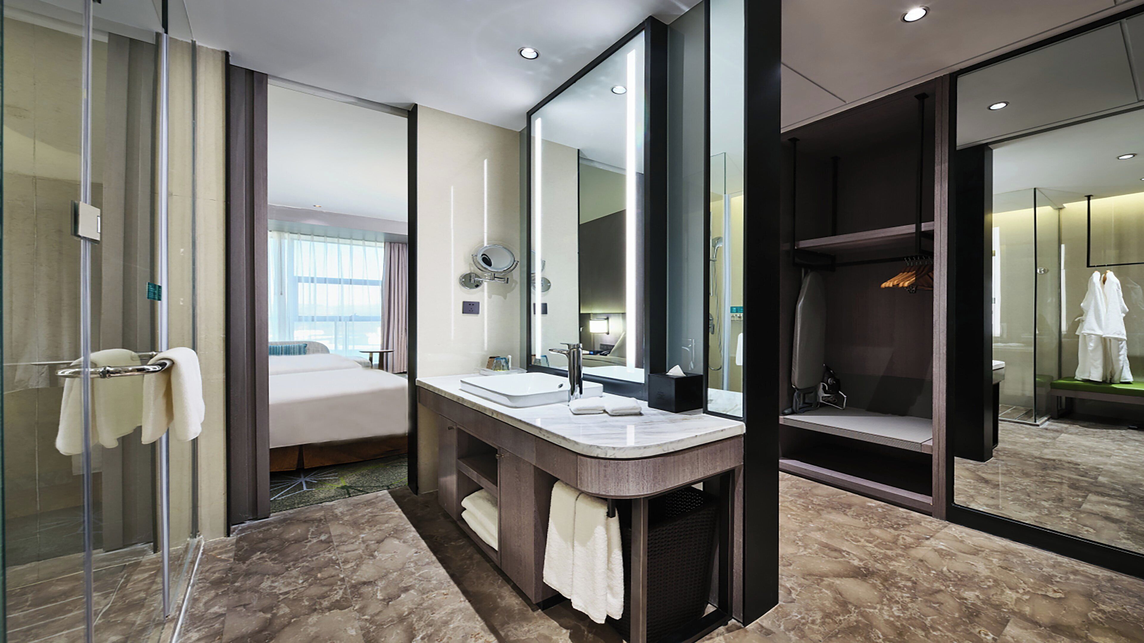 Un baño de hotel moderno con cabina de ducha de vidrio, tocador doble y un espejo grande.