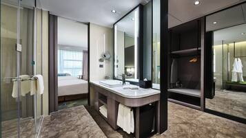 Un baño de hotel moderno con cabina de ducha de vidrio, tocador doble y un espejo grande.