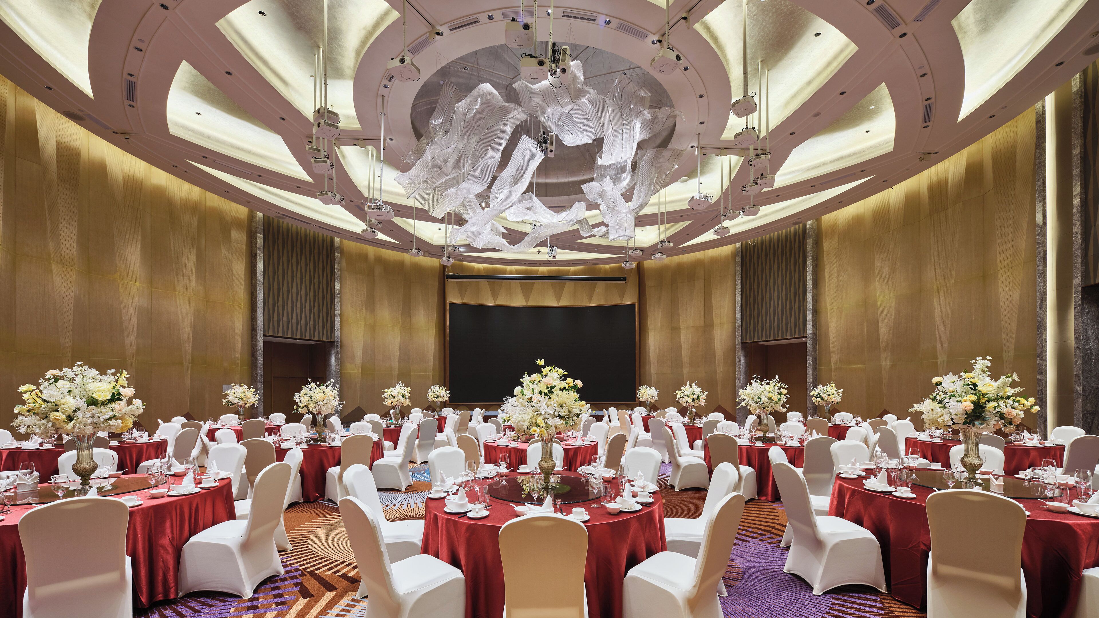 Una sala de banquet amb taules rodones, cadires blanques i centrals florals.