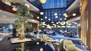 A spacious lobby with a central tree, seating areas, and a modern reception desk.