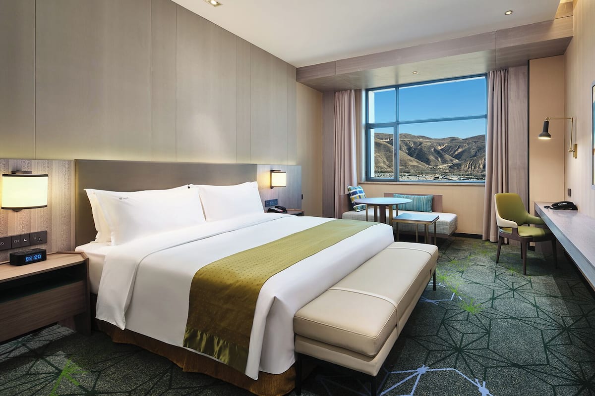 Ein Hotelzimmer mit einem großen Bett, einem Schreibtisch, einem Stuhl, einem Fernseher und Blick auf die Berge.