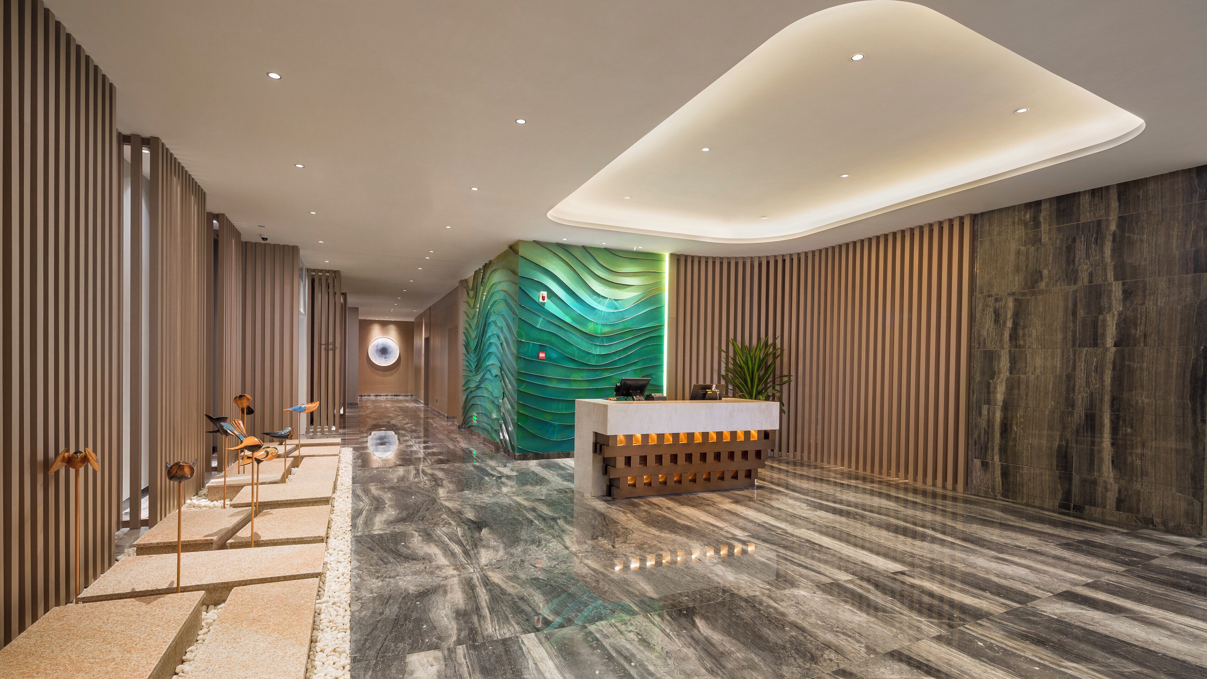 Rebedor modern d'hotel amb taulell de recepció, sòl de marbre i paret verda amb textura única.