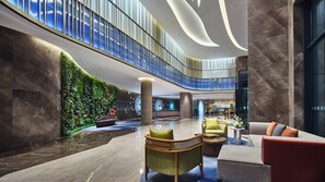 A spacious lobby with a high ceiling, a green vertical garden, and modern seating arrangements.
