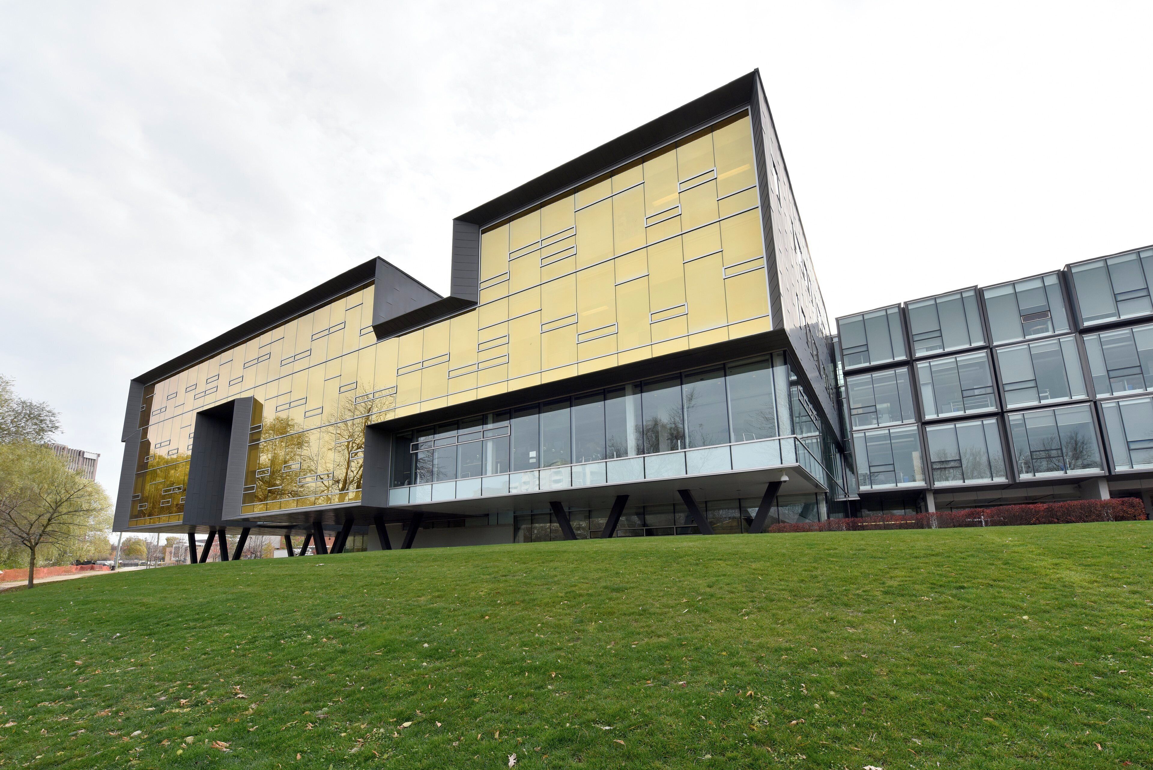 A modern building with a flat roof, large windows, and a grassy area in front.