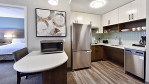 Une cuisine moderne équipée d’un réfrigérateur, d’un four à micro-ondes et d’un lave-vaisselle, tous en acier inoxydable. On y trouve une table à manger avec des chaises, un lit avec vue et un tableau accroché au mur.