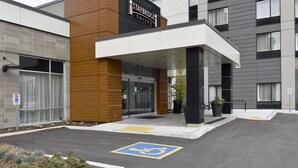A modern hotel entrance with a covered walkway, a sign indicating a no parking zone, and a handicapped parking space. - Staybridge Suites Waterloo - St. Jacobs Area by IHG (Township of Woolwich)
